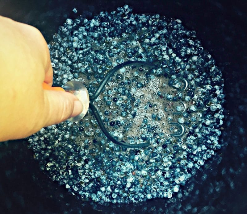 smashing the elderberries in a crock with a potato masher