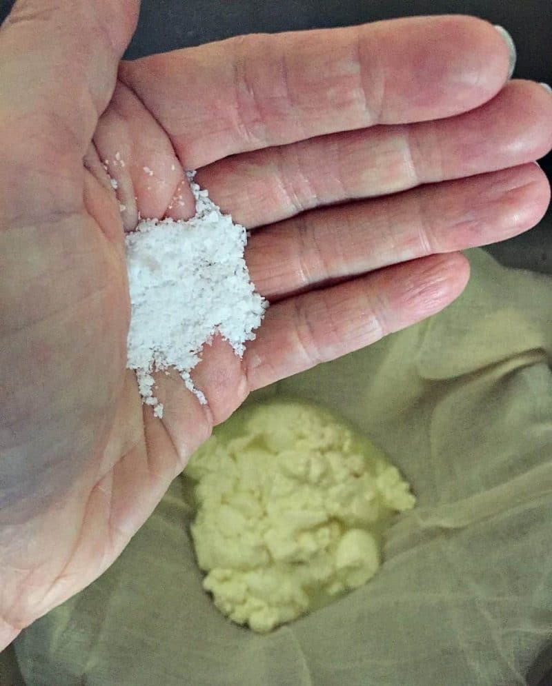 a hand adding salt to the cheese curd layers