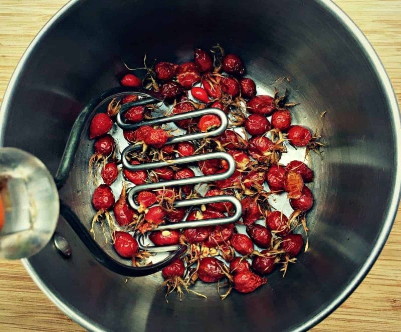 potato masher crushing rose hips in a bowl