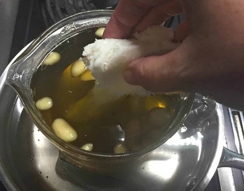 a hand adding the shea butter to the oil mixture