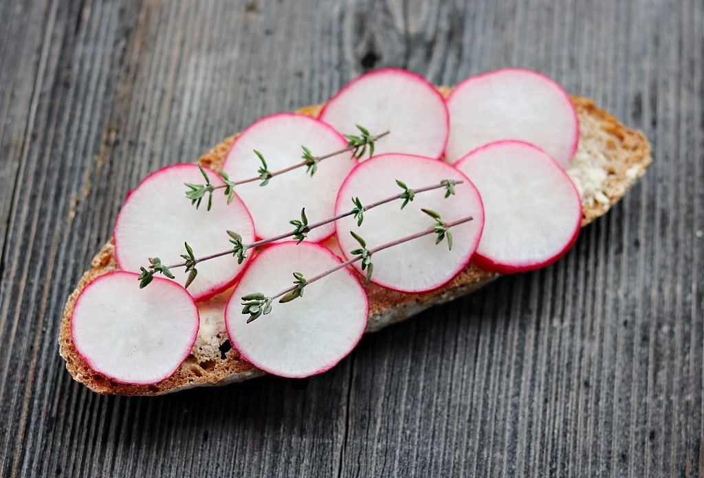 a slice of bread with butter, sliced radishes, and fresh thyme