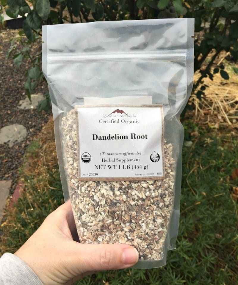 a hand holding a bag of dried dandelion root from mountain rose herbs