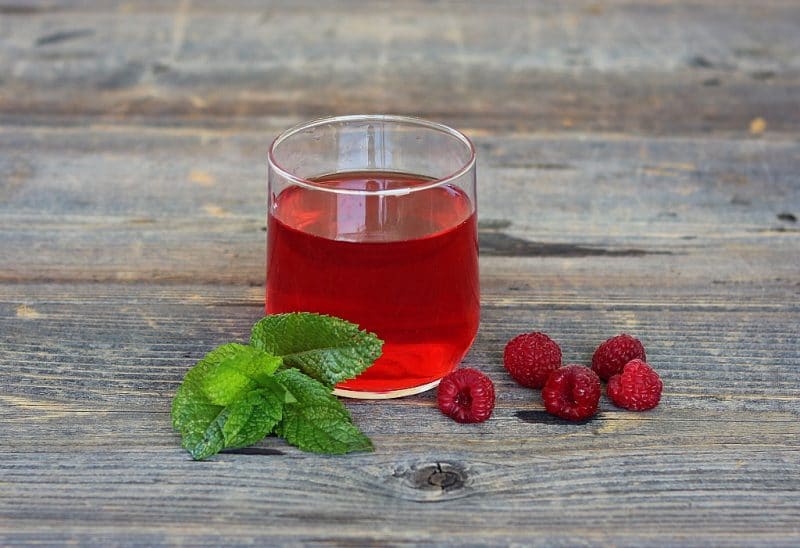 a glass of raspberry mint infused wine with a mint sprig and fresh raspberries