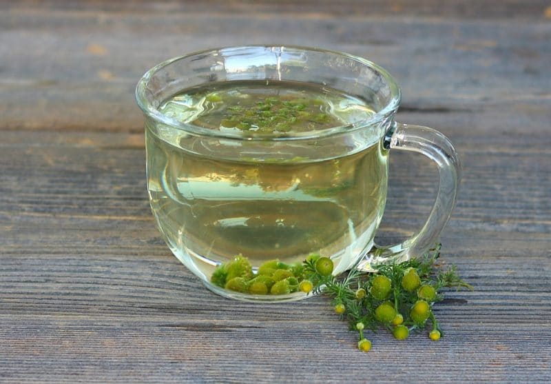 a glass mug of pineapple weed tea on a wooden table