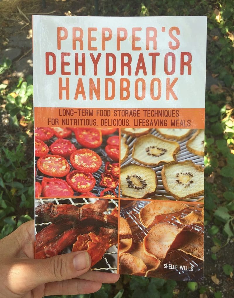 a woman's hand holding the prepper's dehydrator handbook