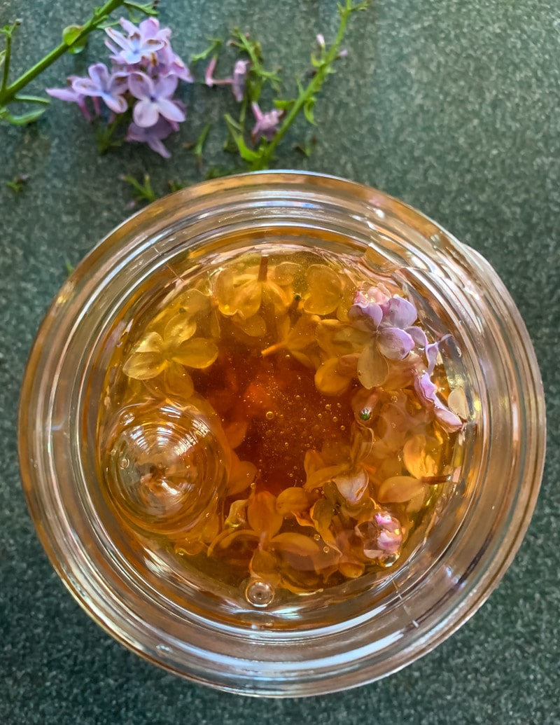 honey bubbling up in the jar with lilac flowers