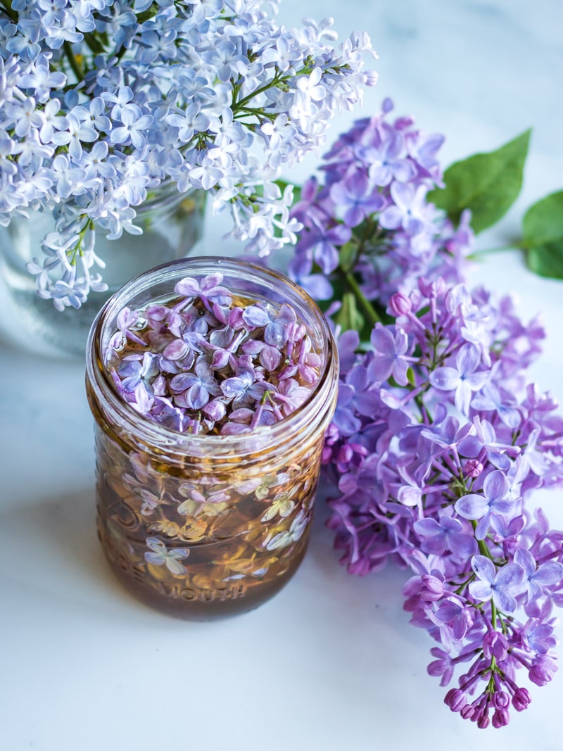 a jar of lilac flower honey with with and purple lilac blossoms
