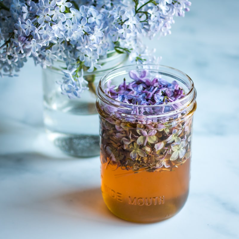 a jar showing the lilac blossoms floating to the top of the honey
