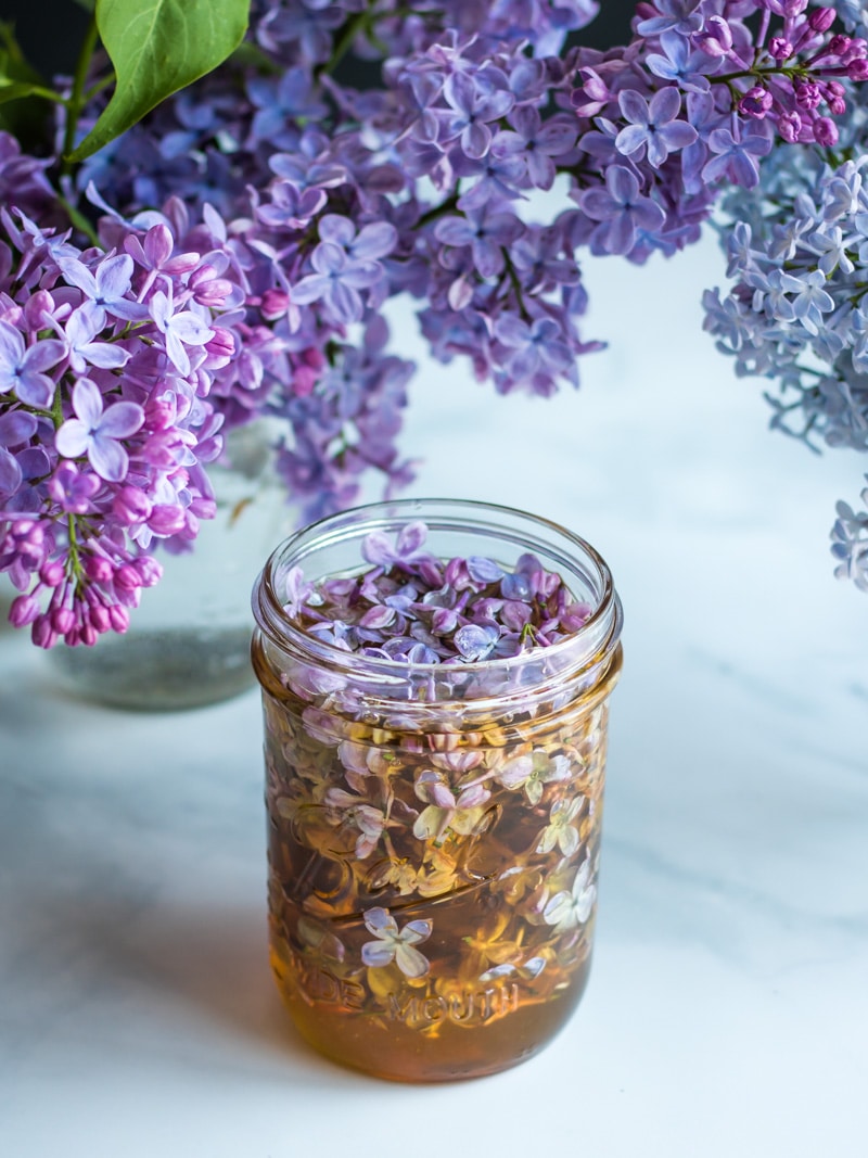 a jar of lilac infused hone with lilac flowers all around