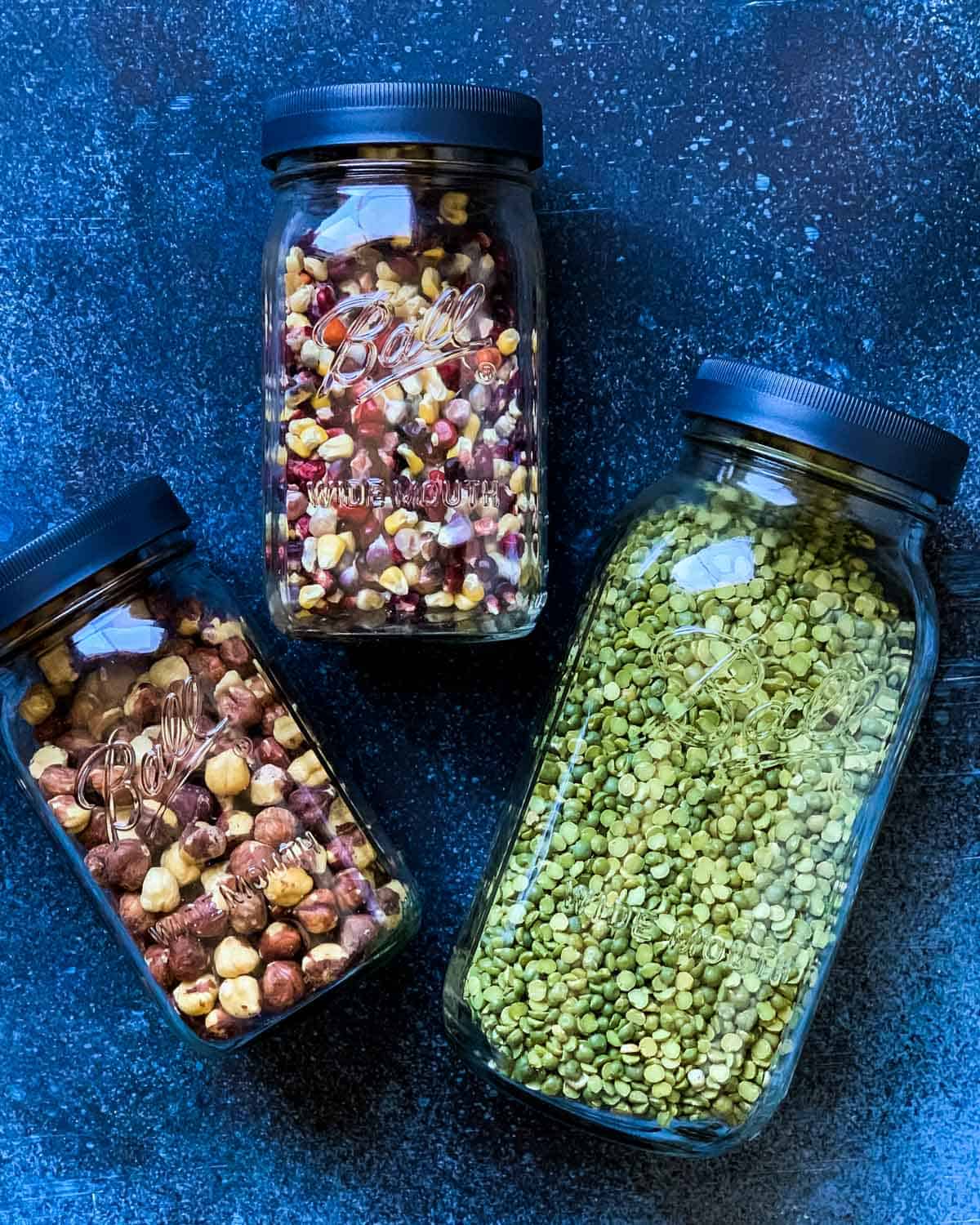 three ball jars filled with popcorn, nuts, and beans