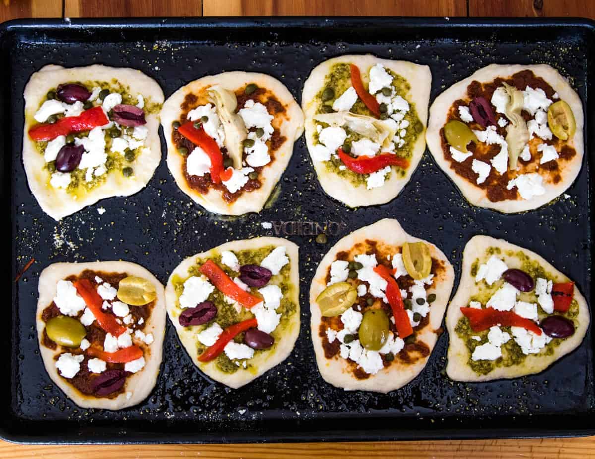 mini sourdough pizzas on a sheet pan waiting to be baked