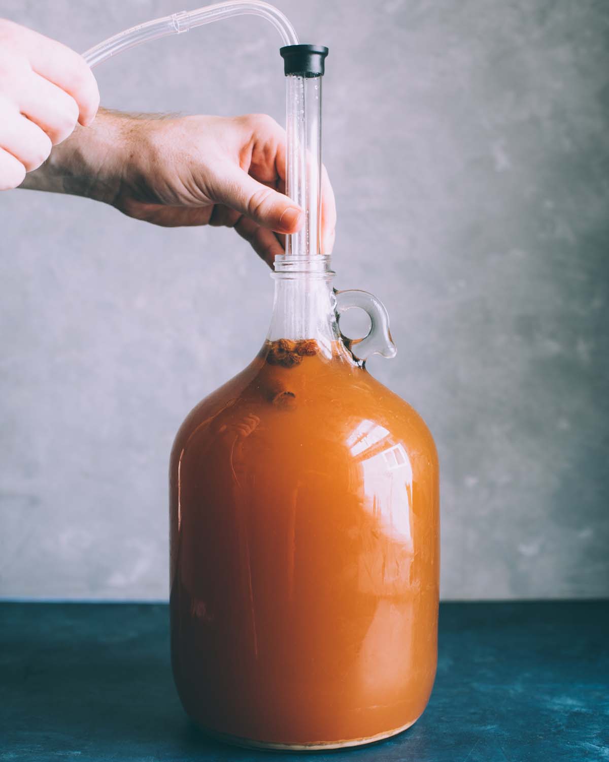 a hand putting the auto siphon into the jug of cider