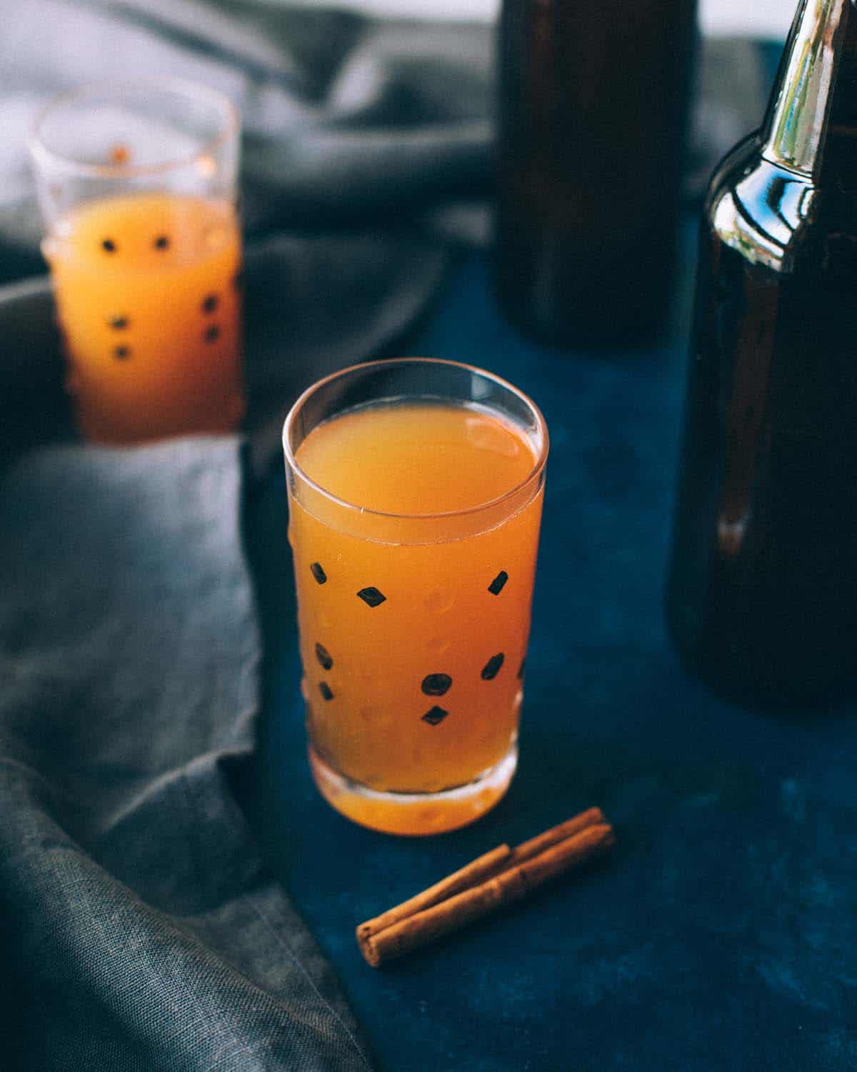 a glass of hard cider on a table with a cinnamon stick