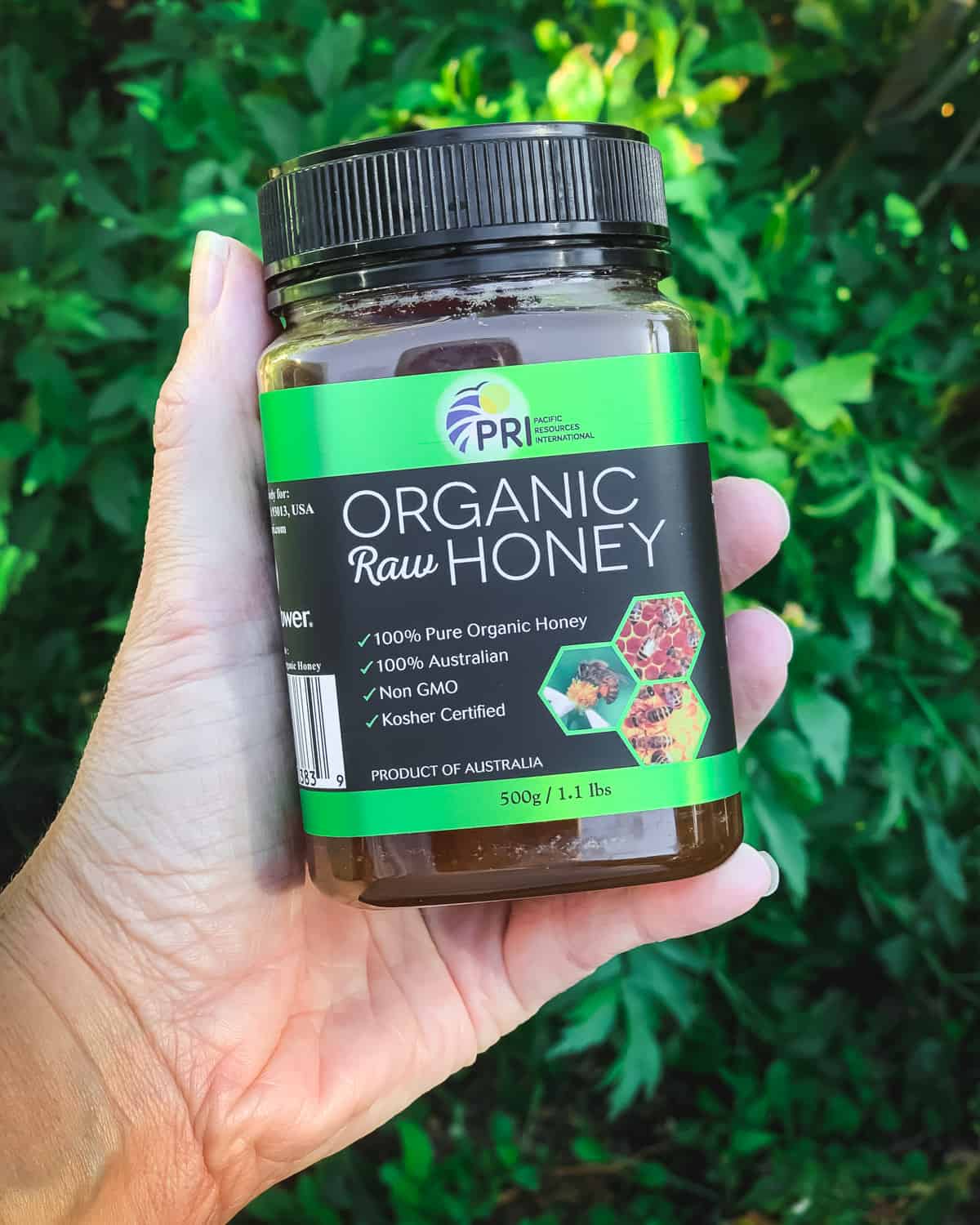 a hand holding a container of organic raw honey from pri