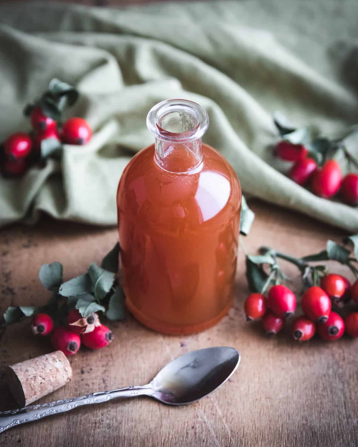 a bottle of rose hip syrup on a table with a spoon