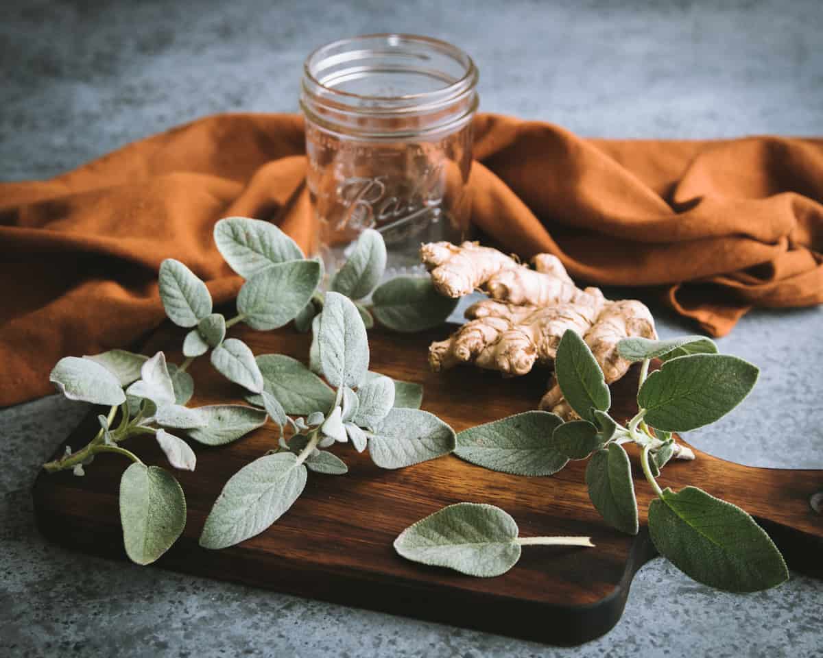 fresh sage and ginger on a cutting board with a ball jar