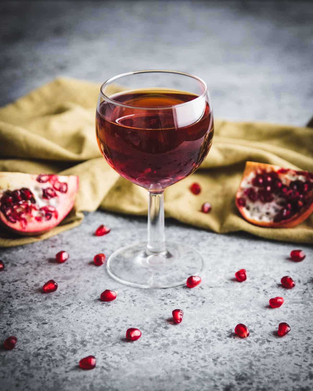 a glass of pomegranate wine on a table with pomegrante seeds