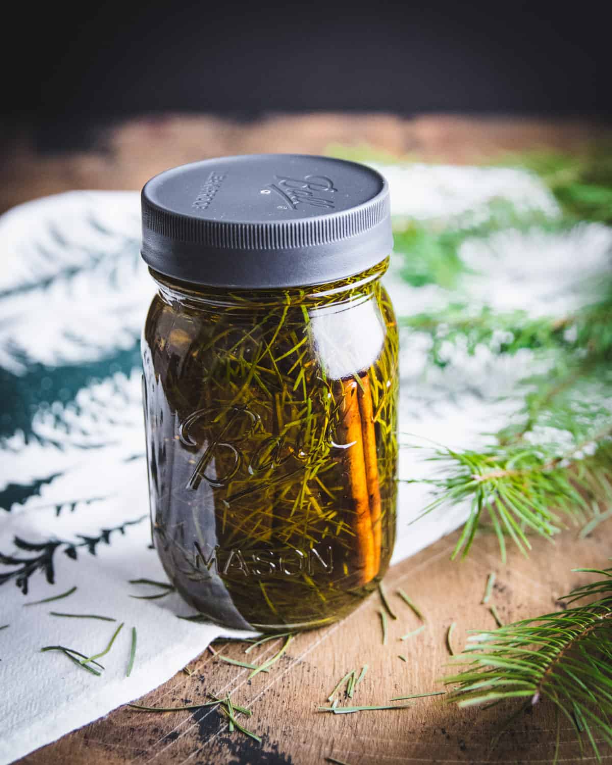 a jar of conifer infused oil with a cinnamon stick