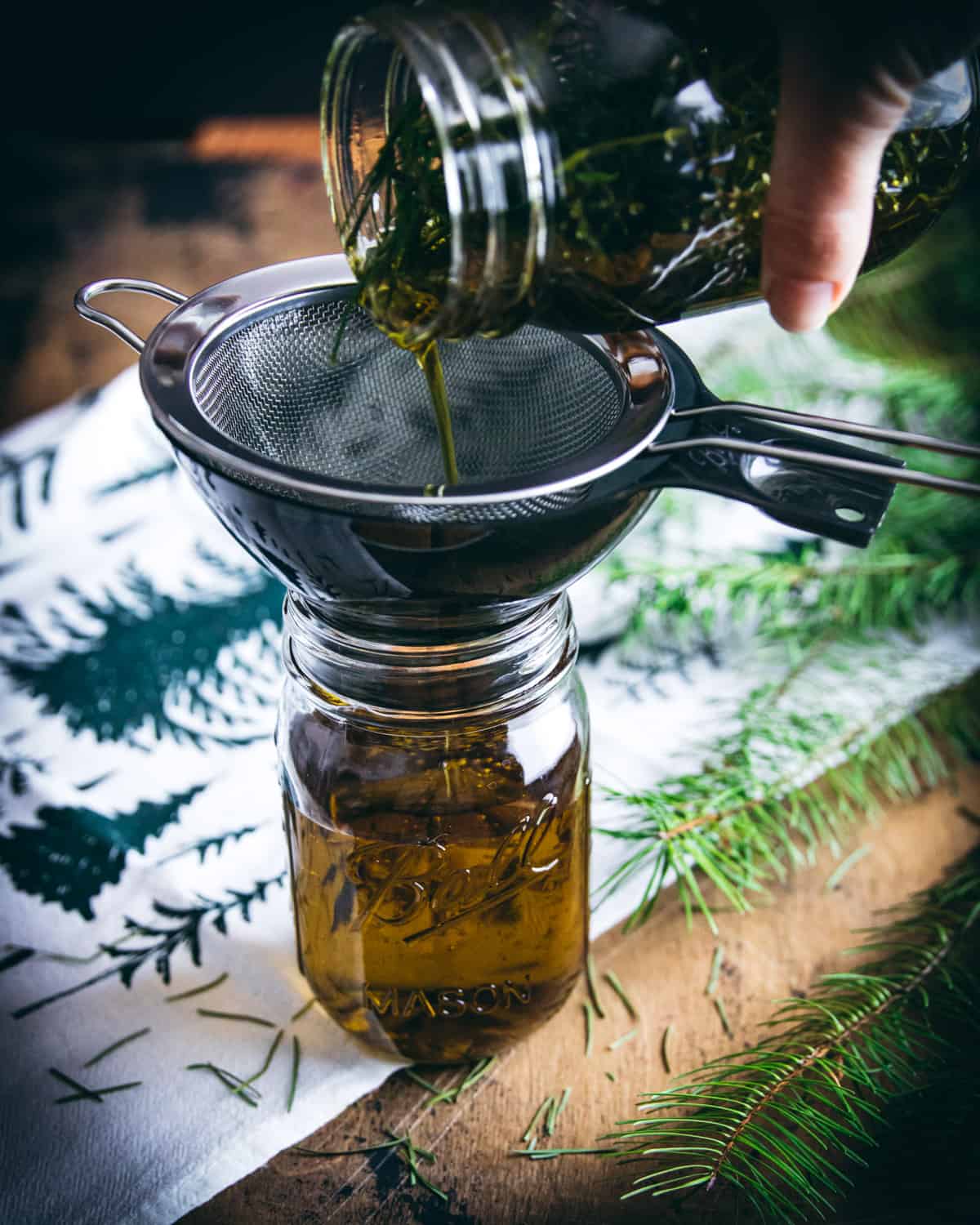 pouring the conifer infused oil through a strainer