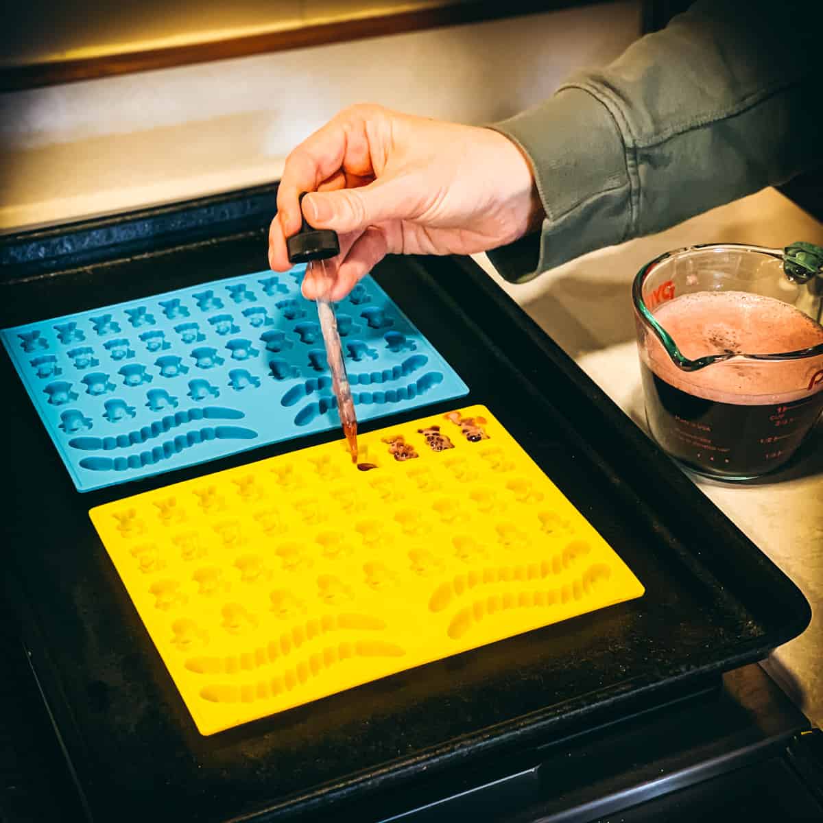 a woman using a dropper to fill elderberry gummy molds