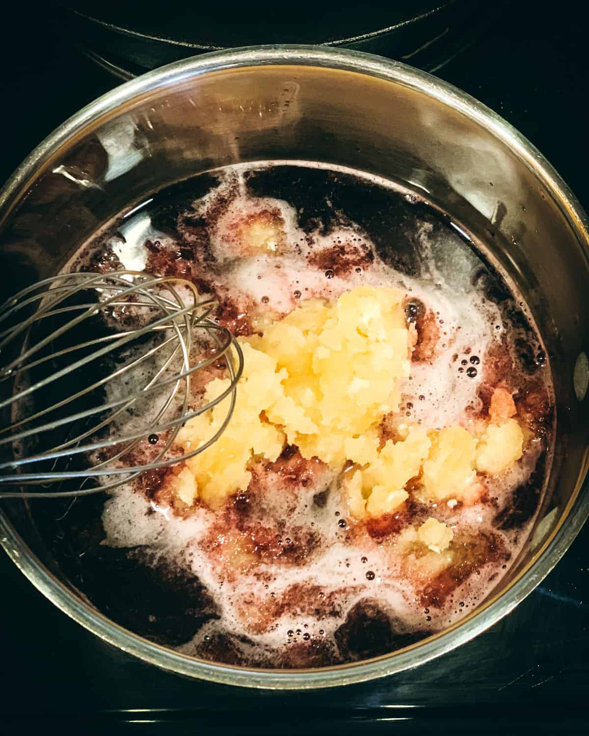 a whisk stirring the gelatin mixture into the elderberry syrup