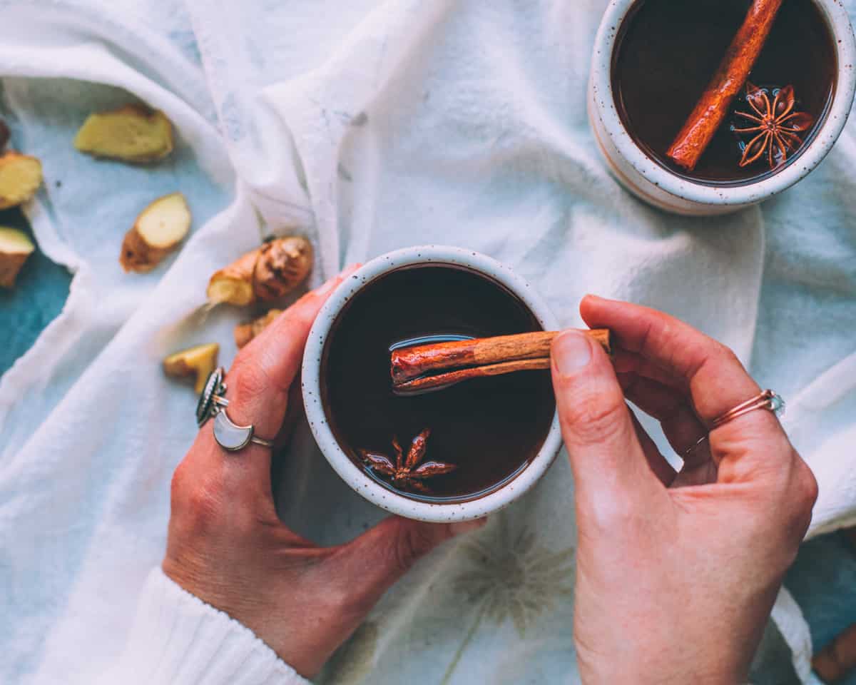 a woman's hands holding a mug of black chai with a cinnamon stick