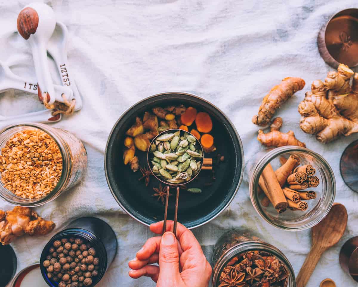 a hand holding a measuring cup full of cardamom pods to go in the pot of chai spices