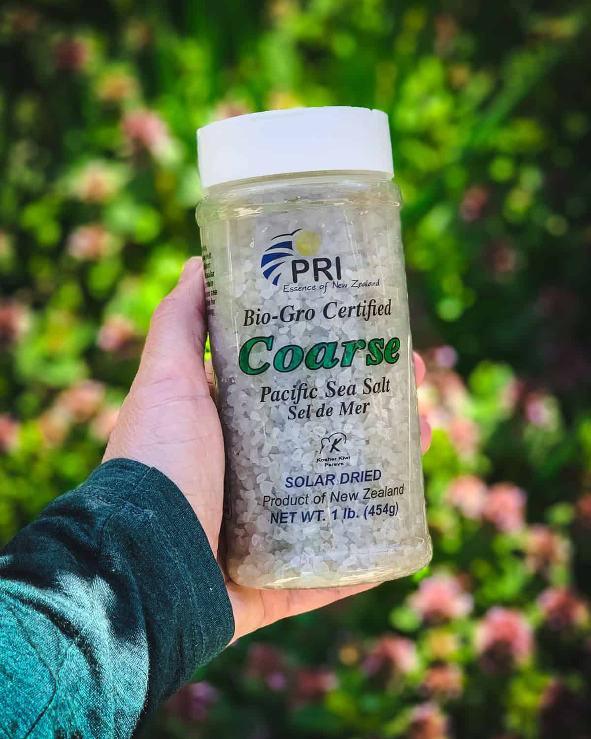 a hand holding a container of PRI coarse sea salt