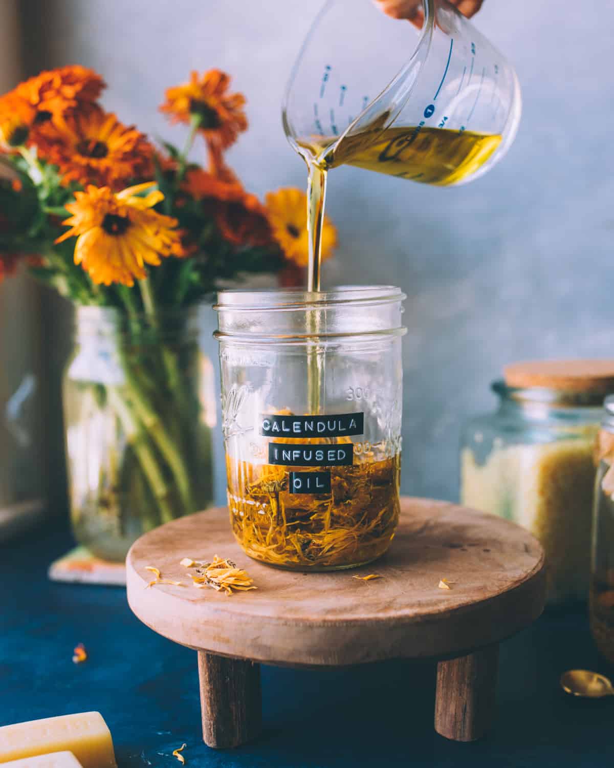 a hand pouring oil into a jar with dried calendula flowers