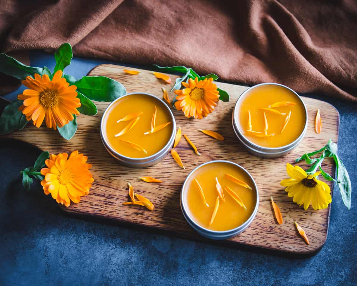 homemade calendula salve on a wooden cutting board with flowers