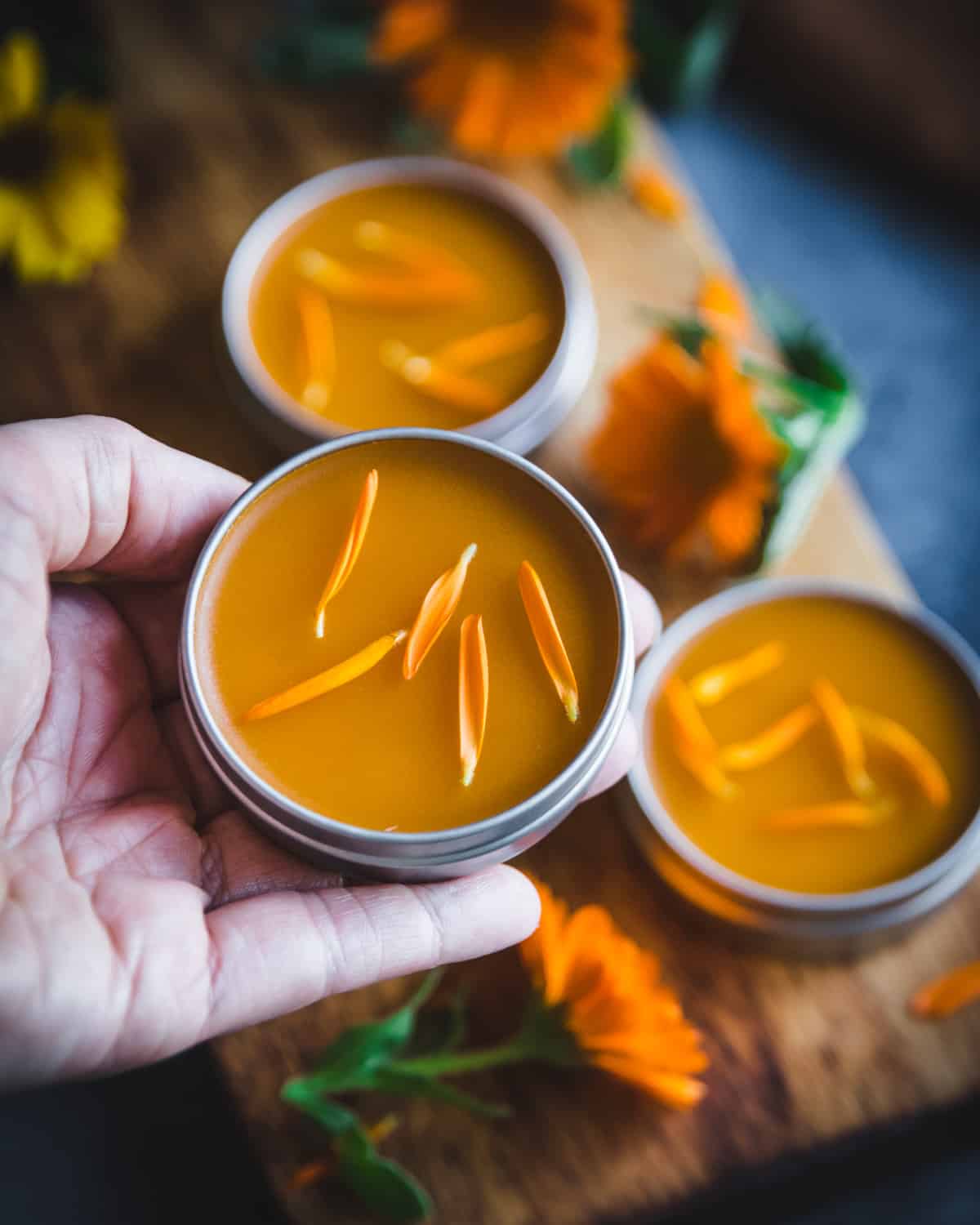 a hand holding a tin of homemade calendula salve