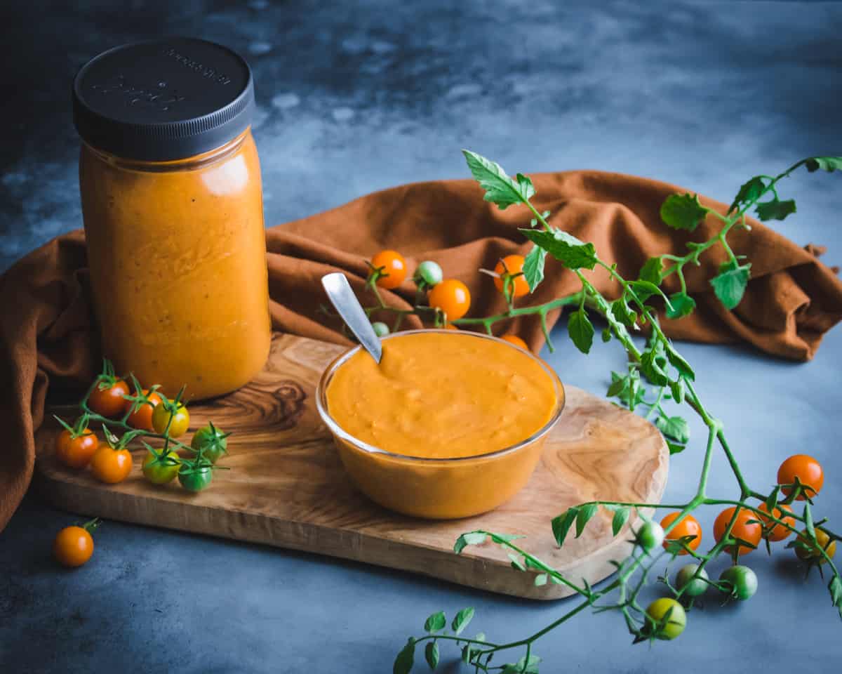 a bowl and a jar of roasted cherry tomato sauce on a wooden board