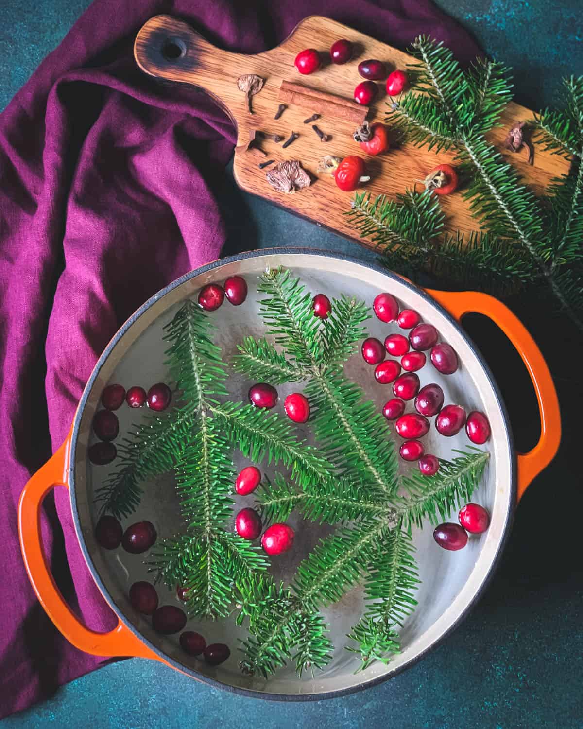 a pot filled with water, cranberries, and conifer sprigs